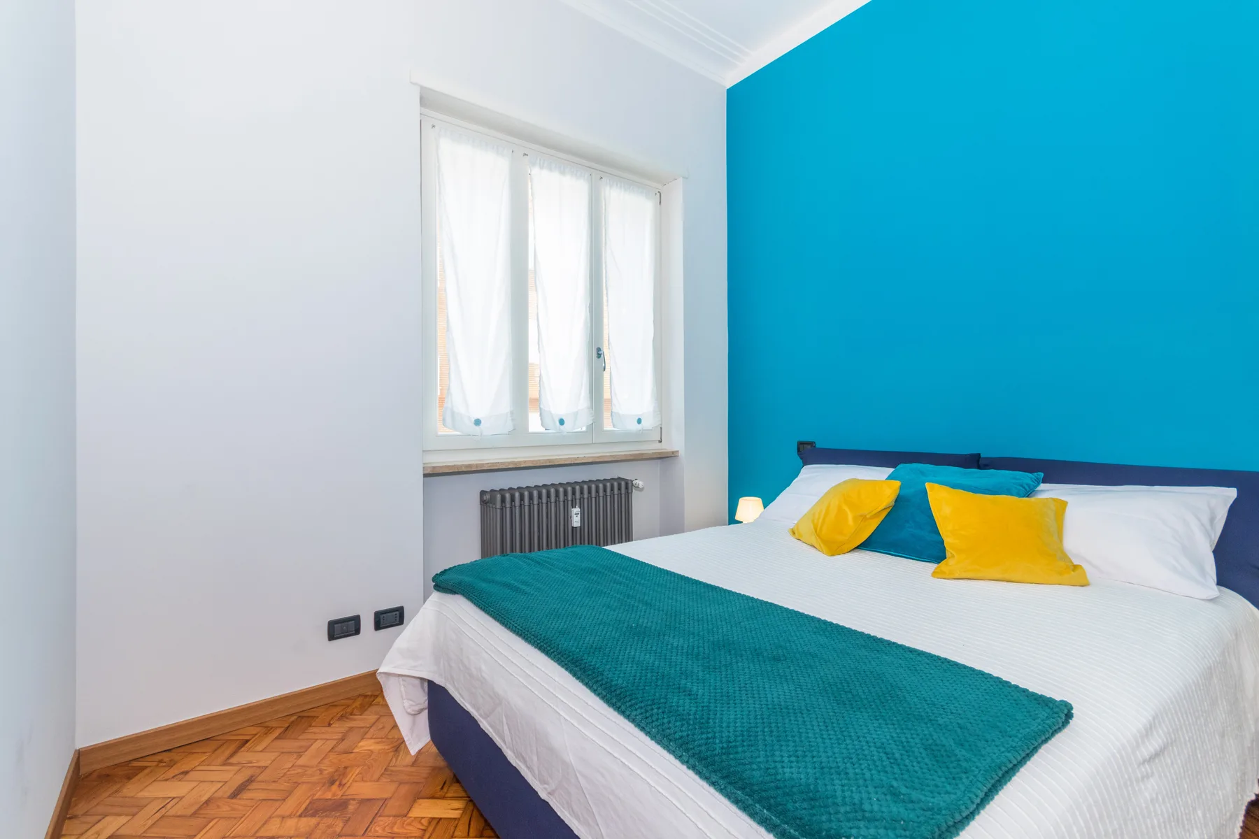 A bedroom with a bed, colorful pillows, and a bright blue accent wall.