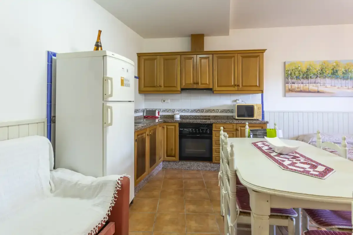 Una cocina y comedor con armarios de madera, electrodomésticos y una mesa.