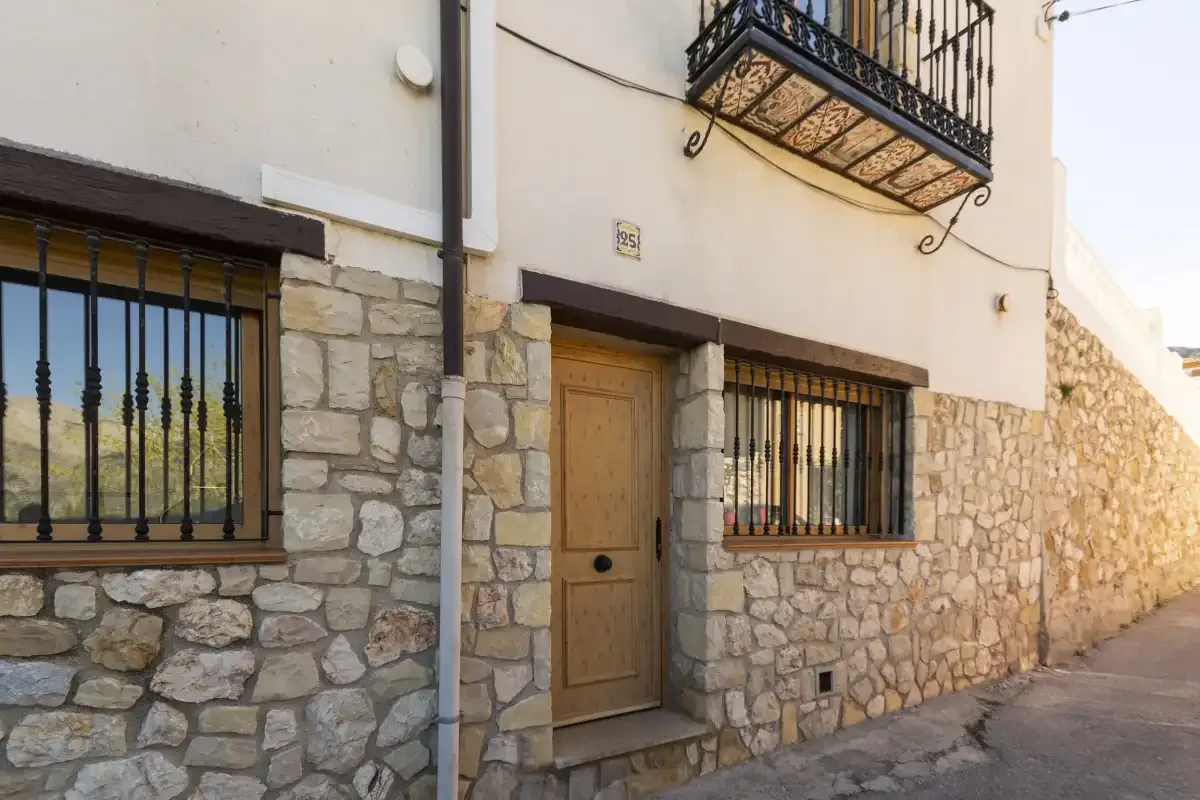 Una casa con fachada a la calle tiene una puerta de entrada de madera y ventanas con rejas.
