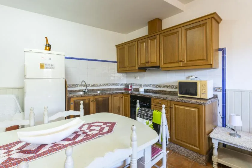 Una cocina con gabinetes de madera, un refrigerador y una mesa de comedor.