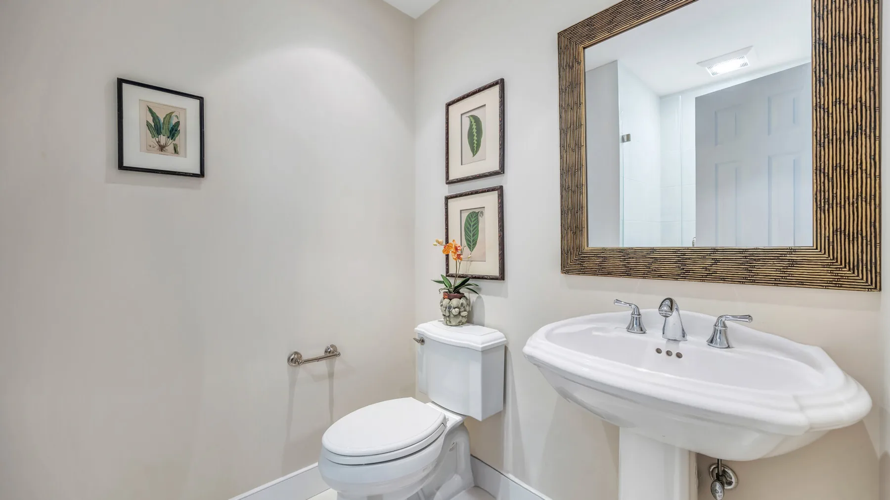 Un baño con lavabo de pedestal, inodoro y un gran espejo enmarcado.