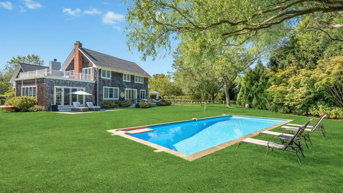 A landscaped backyard features a swimming pool beside a large house.
