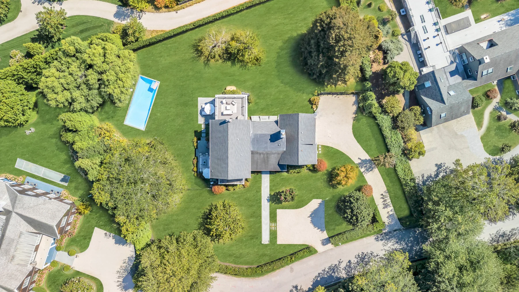 Vista aérea de una propiedad ajardinada con una casa, césped y piscina.