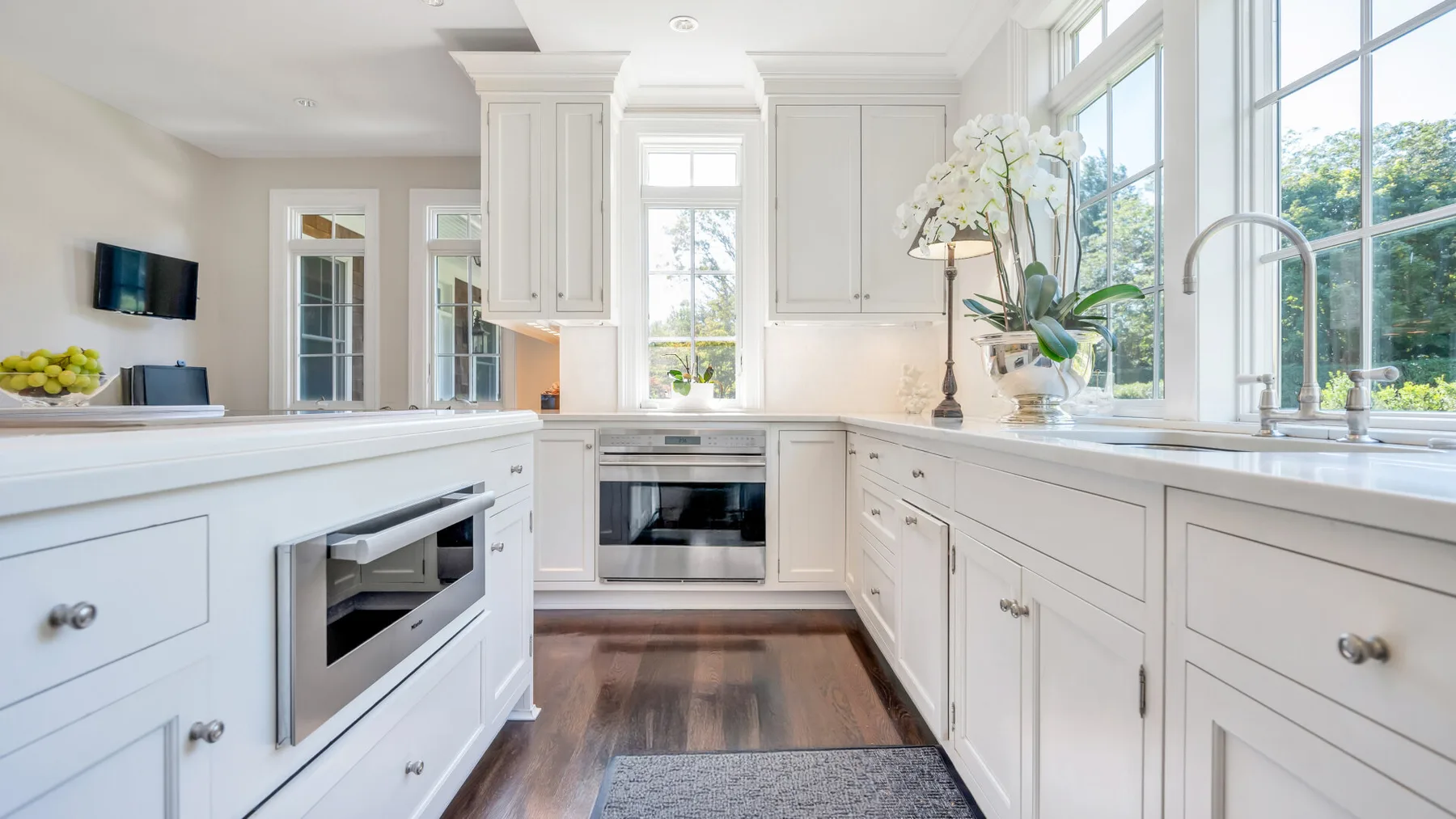 Una cocina blanca y luminosa con una isla central y grandes ventanas.