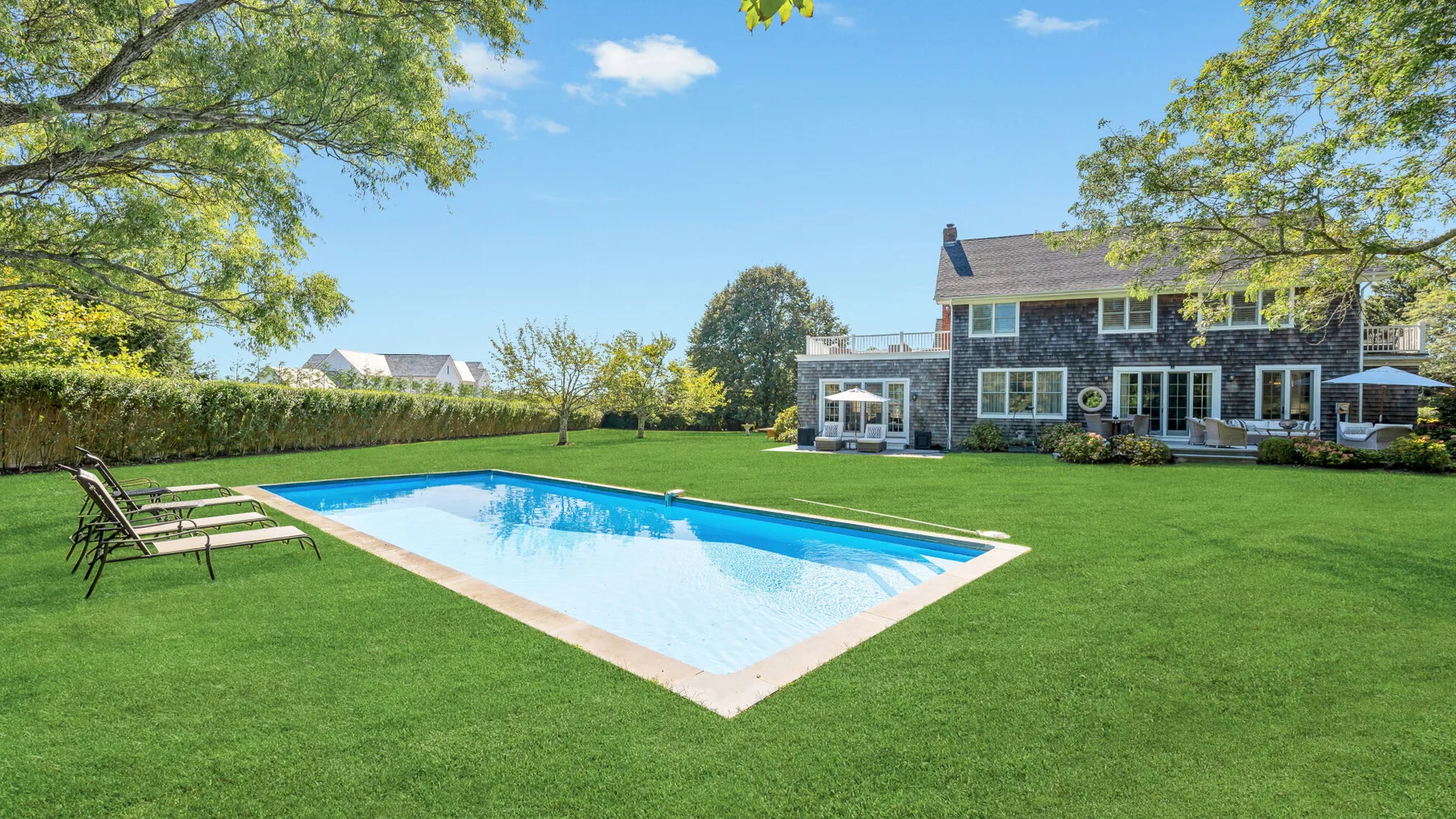Piscina exterior junto a un amplio césped y una casa de dos plantas.