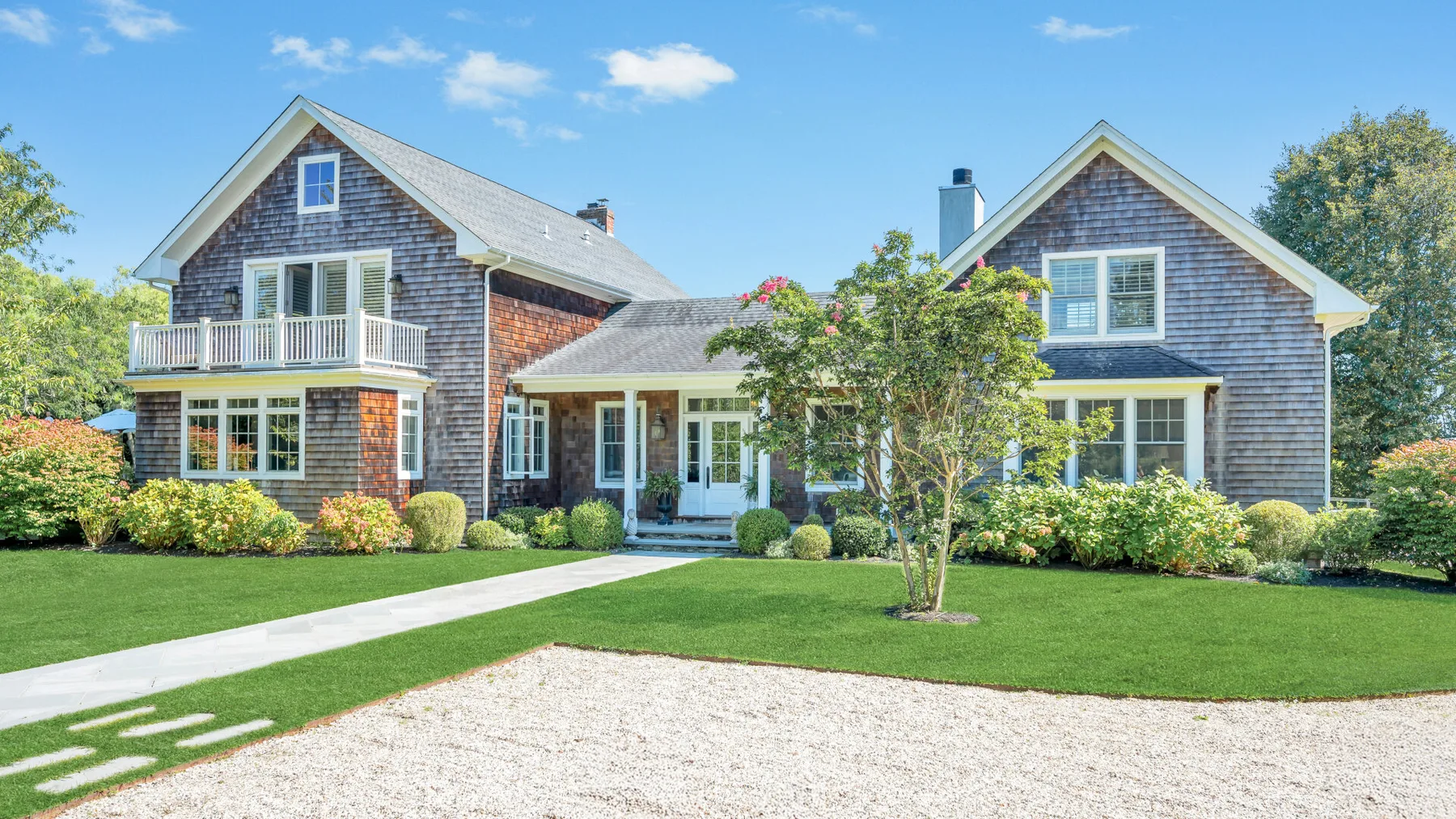 A large house with gray shingle siding, white trim, and a green lawn.