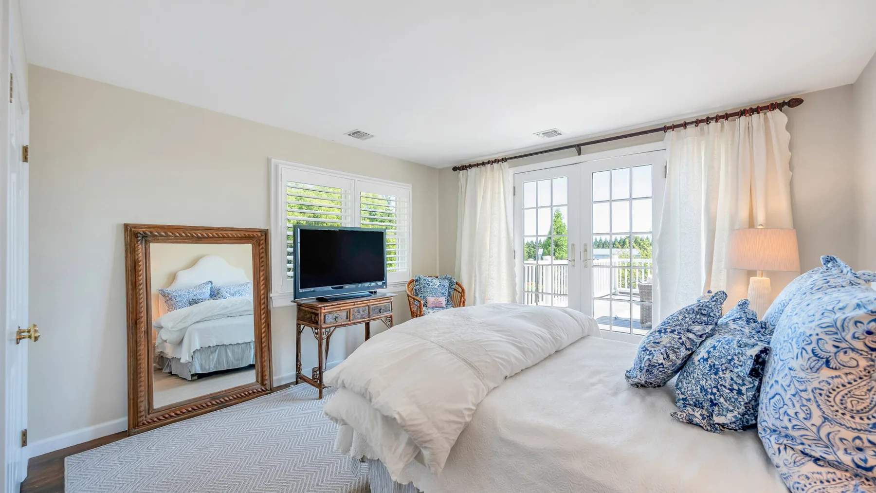 Un dormitorio luminoso con una cama, cojines decorativos y puertas de vidrio que dan a un balcón.