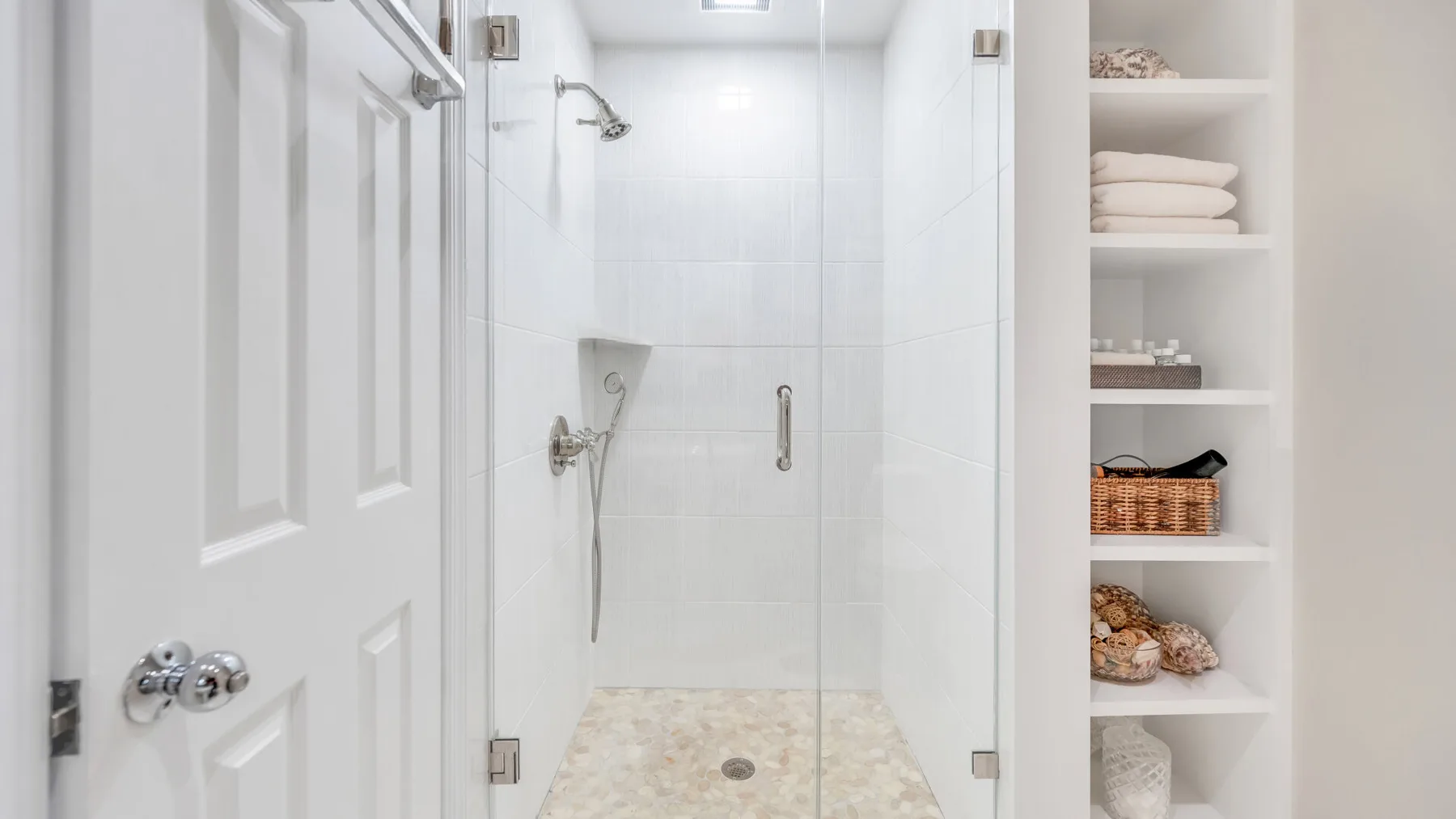 Un baño luminoso con ducha de vidrio y estantes empotrados.