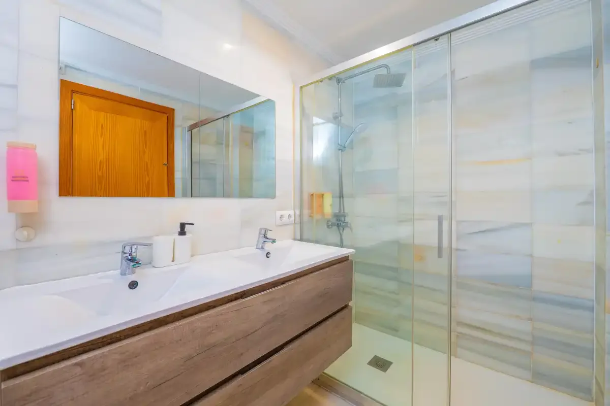 Un baño luminoso con un mueble de lavabo largo y una ducha de vidrio.