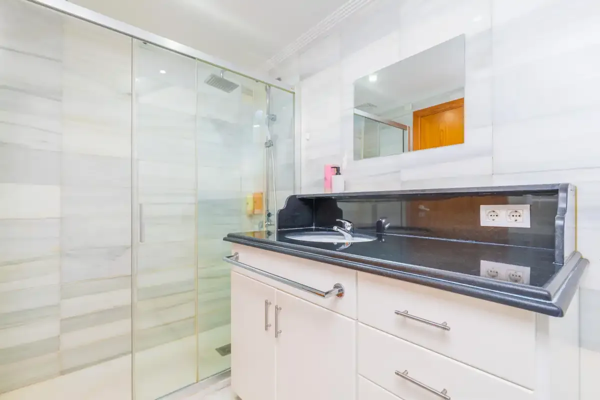 Un baño luminoso con una ducha de cristal y un lavabo con encimera oscura.