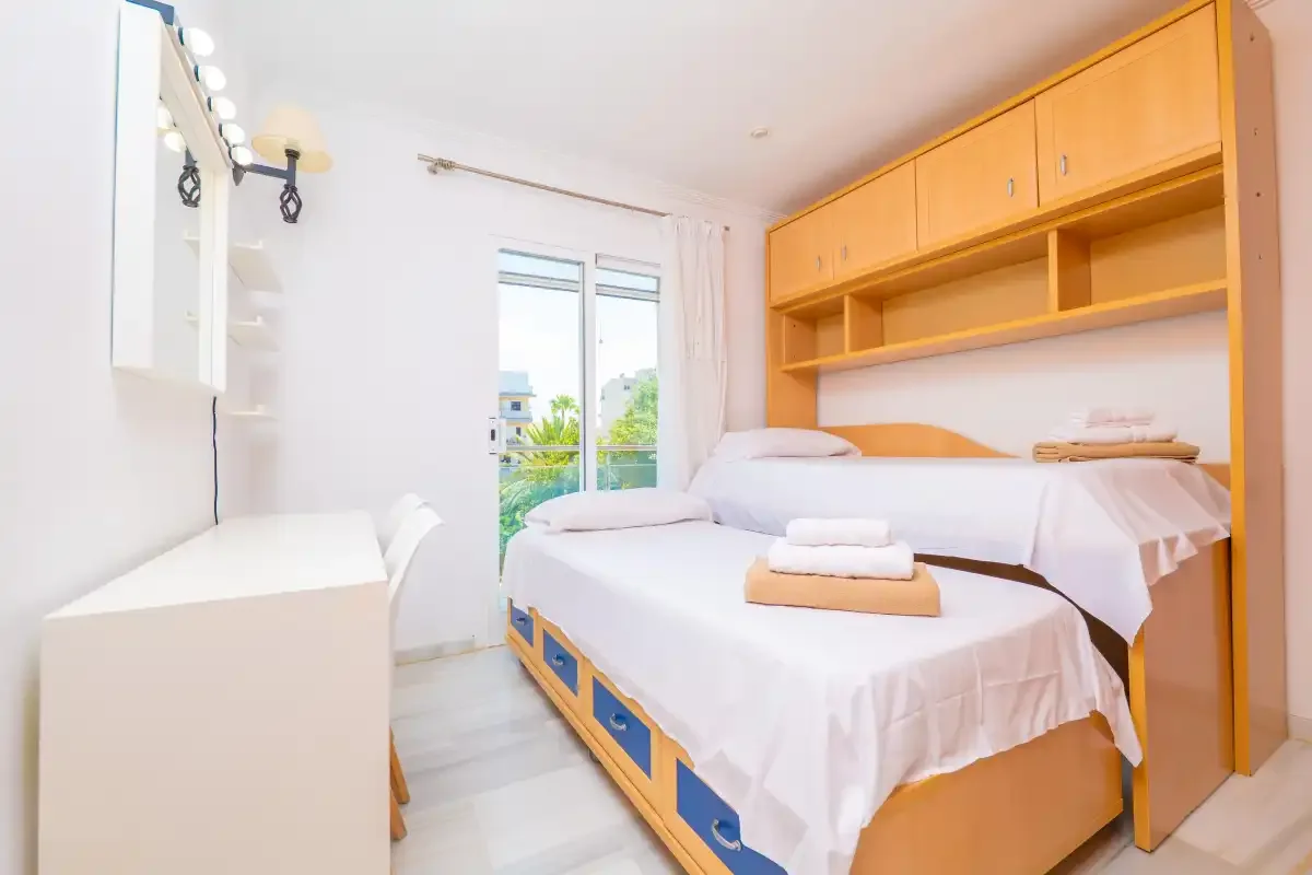 Un dormitorio luminoso con ropa de cama blanca y estanterías de madera.