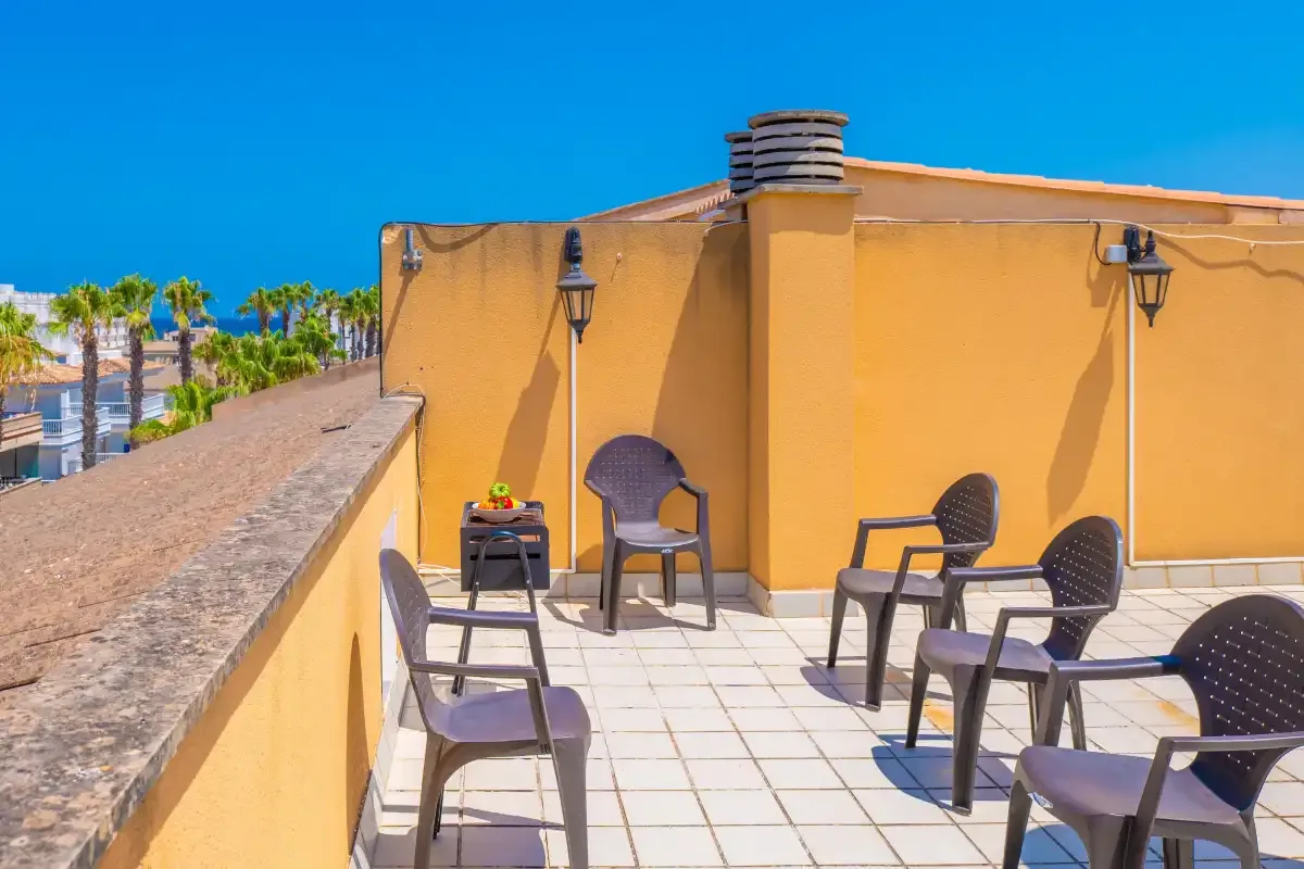 Una terraza soleada en la azotea tiene suelo de baldosas, asientos al aire libre y faroles en la pared.