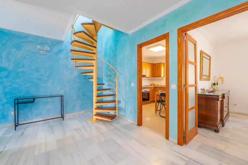 Una habitación turquesa luminosa con una escalera de caracol y puertas abiertas.