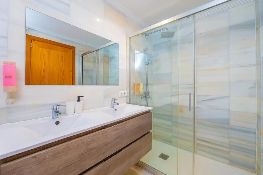 Un baño luminoso con un tocador largo y una ducha de vidrio.