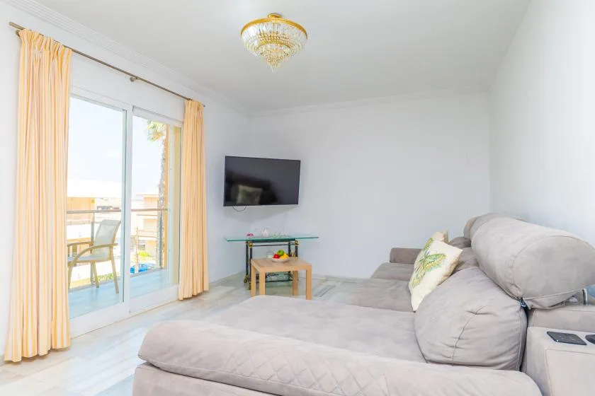 Una sala luminosa con una amplia zona de estar, televisor y puertas de vidrio.