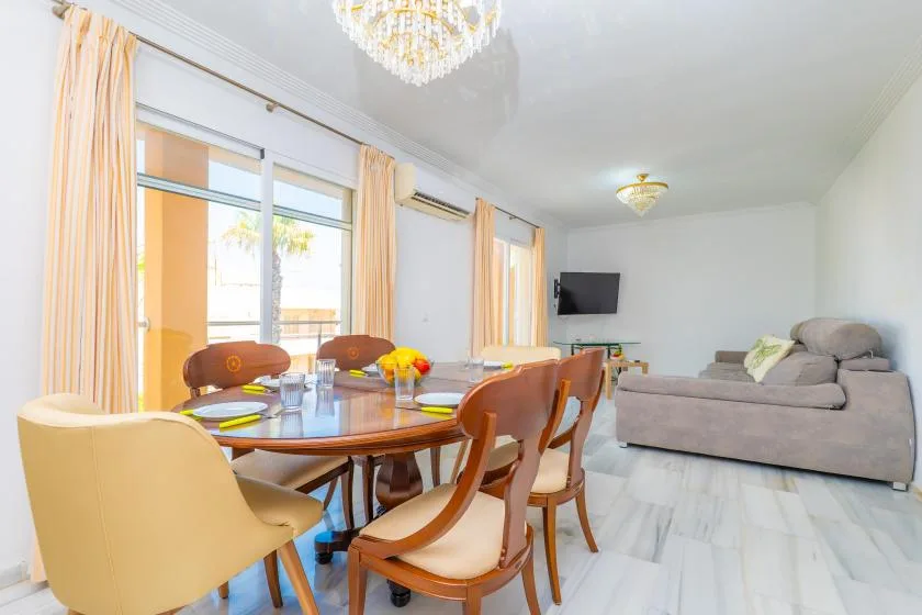 Una luminosa zona de comedor y estar tiene una mesa junto a grandes ventanas y asientos.