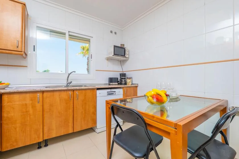 Cocina alicatada con armarios de madera, fregadero y mesa de comedor.