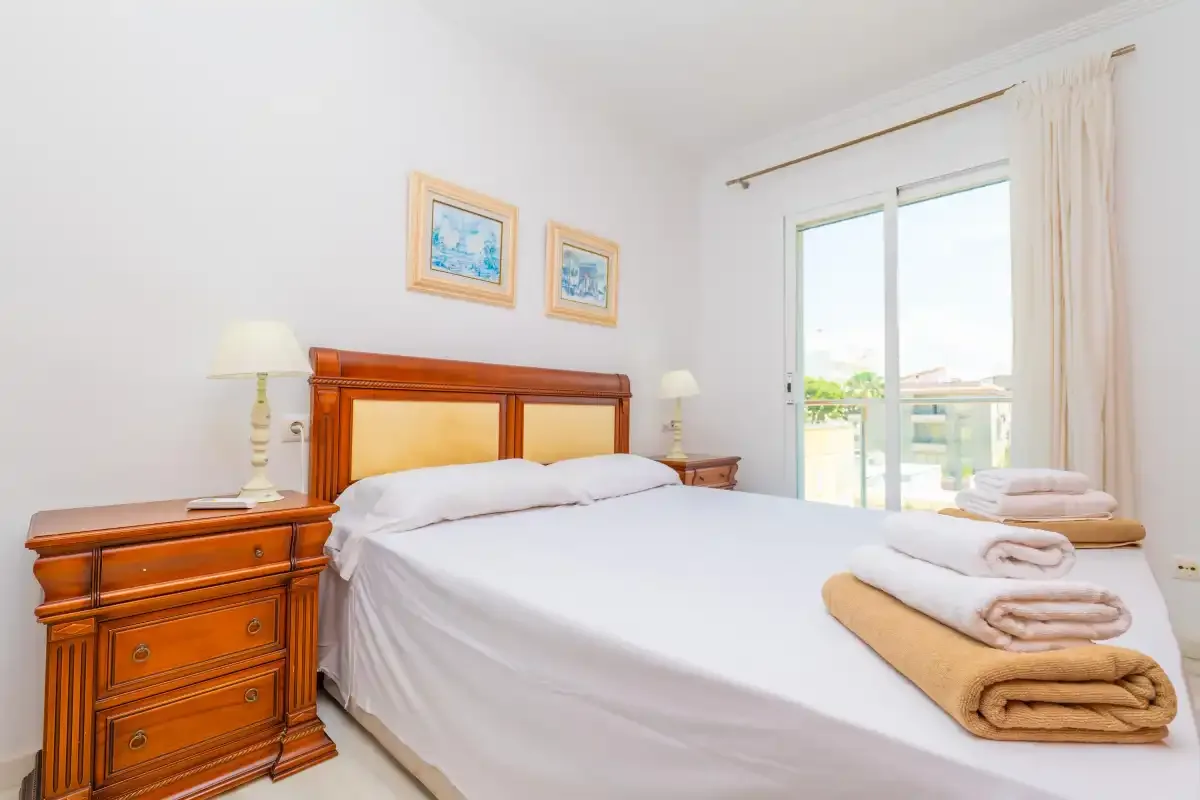 Un dormitorio luminoso con una cama doble y puertas acristaladas que dan a un balcón.