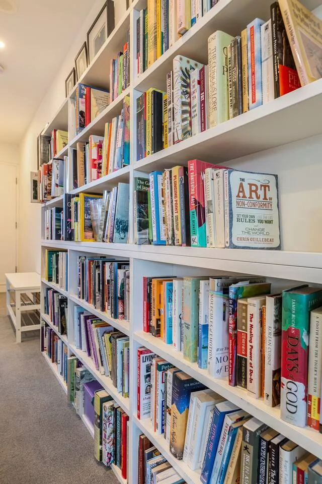 Una estantería alta llena de libros recorre una sala de lectura luminosa.