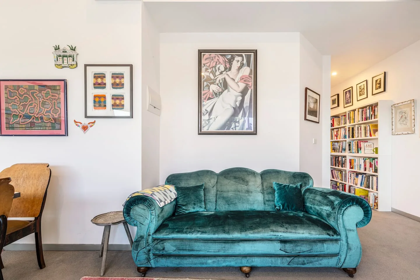 A living room with a teal sofa, framed artwork, and a wall of books.
