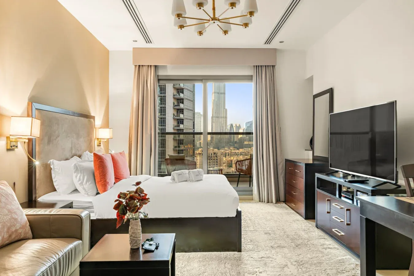 Un dormitorio tipo estudio con cama, asientos y una ventana amplia con vistas a edificios cercanos.