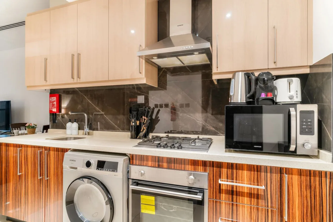 Una cocina compacta con gabinetes claros, una placa de cocción y electrodomésticos sobre la encimera.