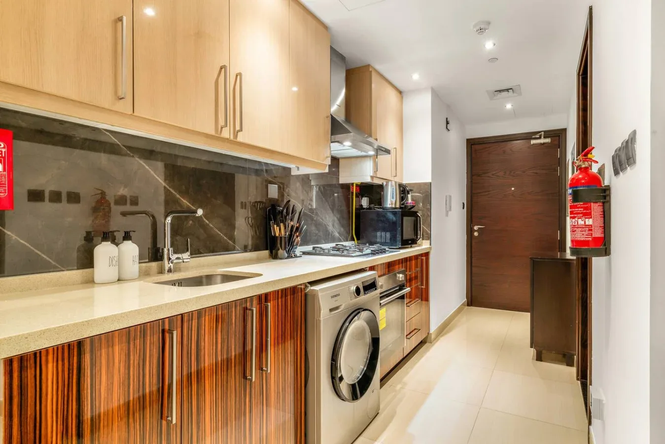 Una cocina alargada con gabinetes de madera clara y una lavadora.