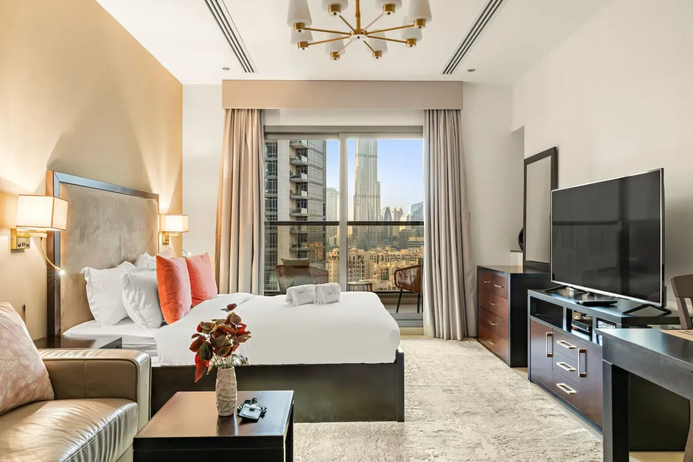 A bright bedroom with a bed, seating, and a large window overlooking city buildings.
