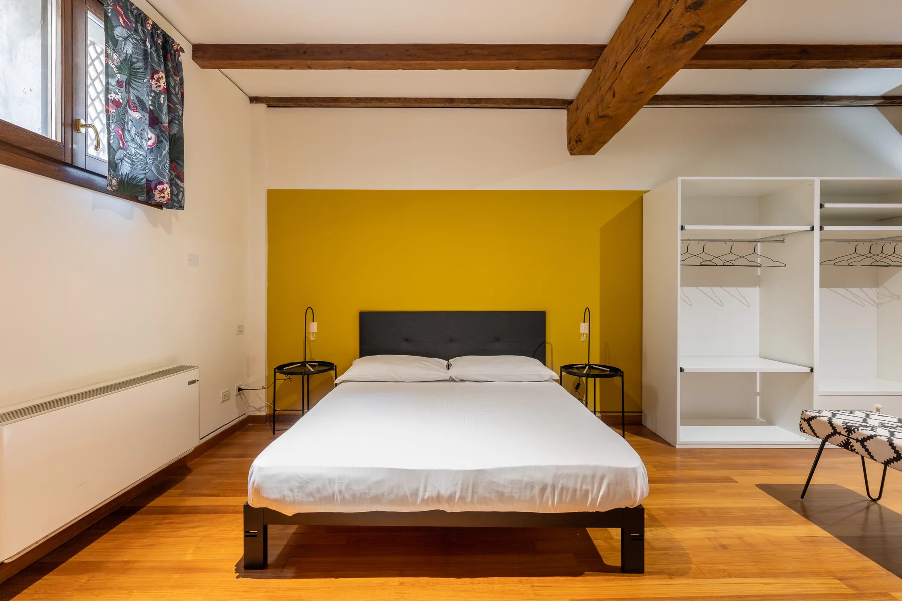 Un dormitorio con una cama frente a una pared amarilla y espacio abierto para guardar ropa.