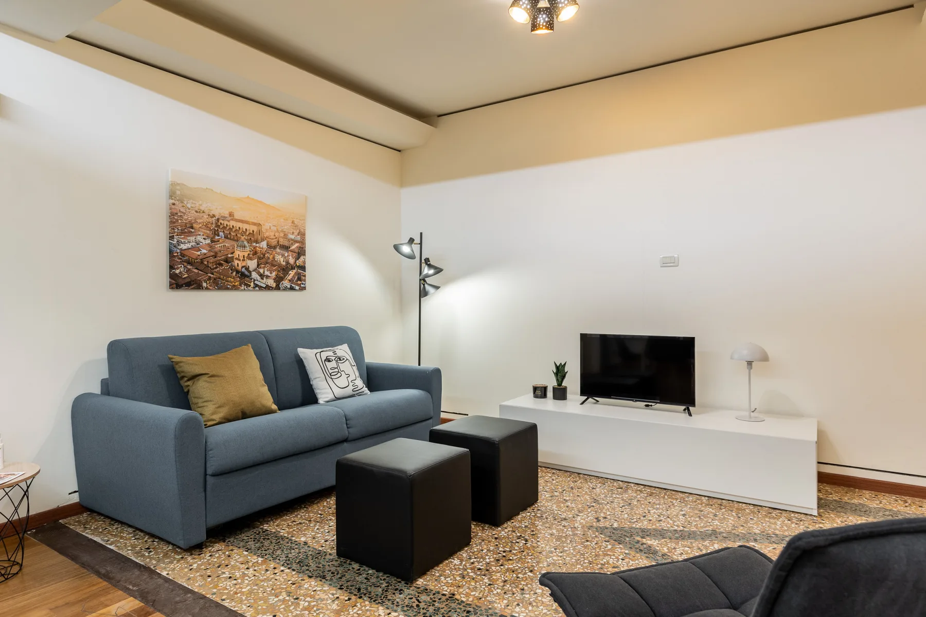 Una sala de estar con asientos azules, un televisor y un mueble bajo blanco.
