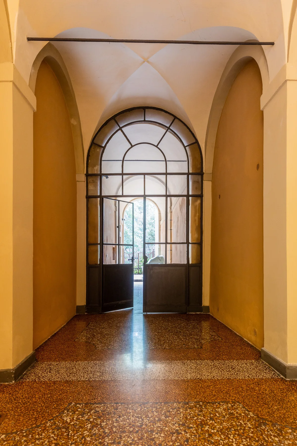 Un pasaje interior con arco, una partición de vidrio con marco metálico y suelo estampado.