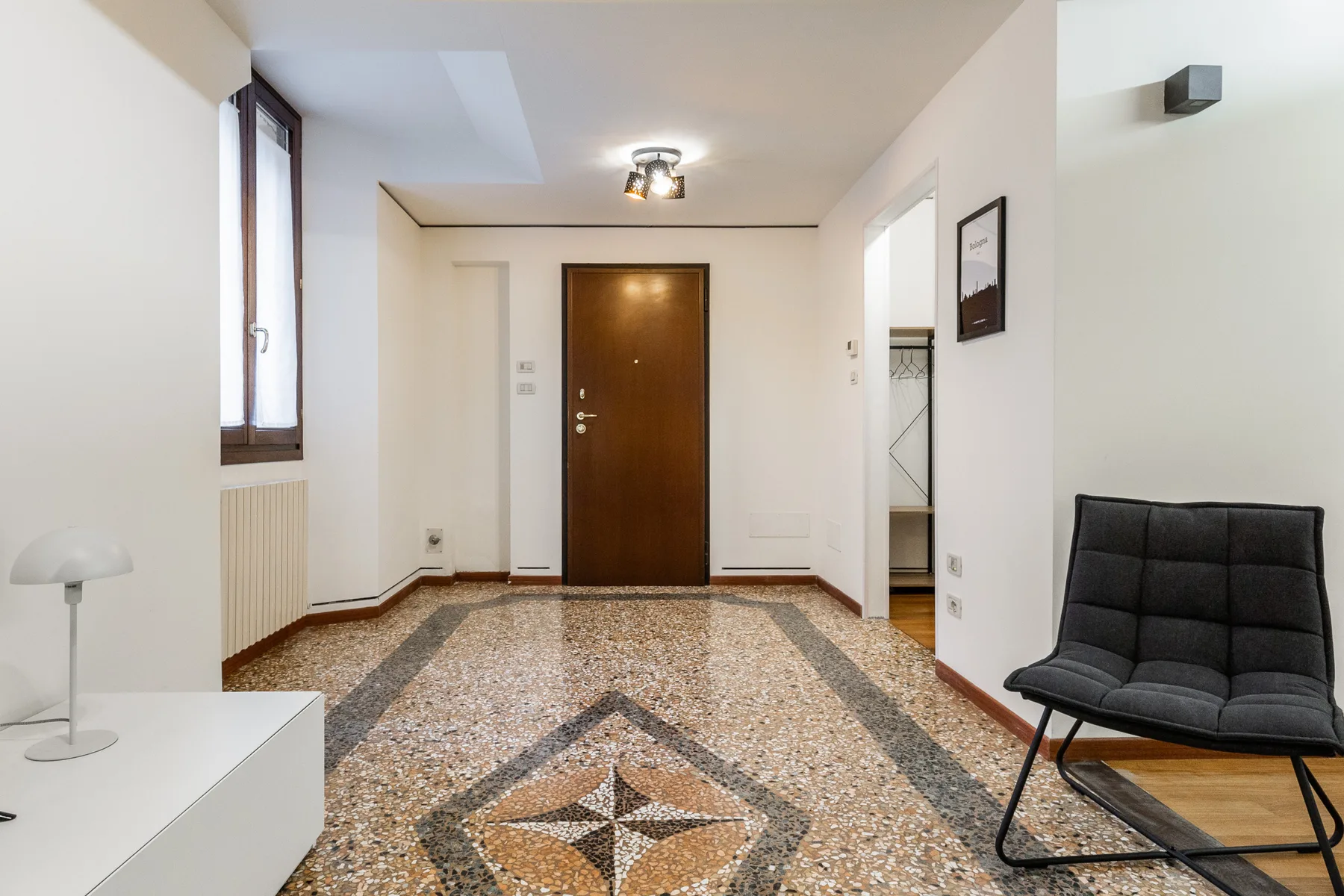 Un pasillo luminoso con suelo de baldosas estampadas y una puerta de entrada oscura.