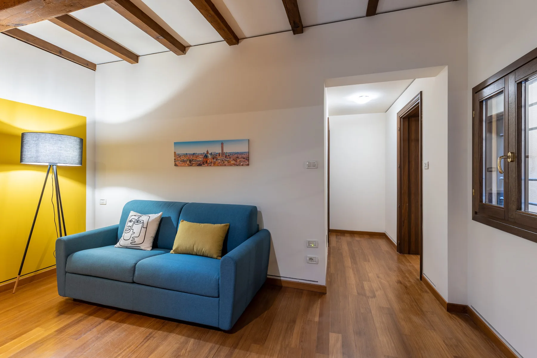Una sala de estar con asientos azules, una lámpara de pie y suelo de madera.