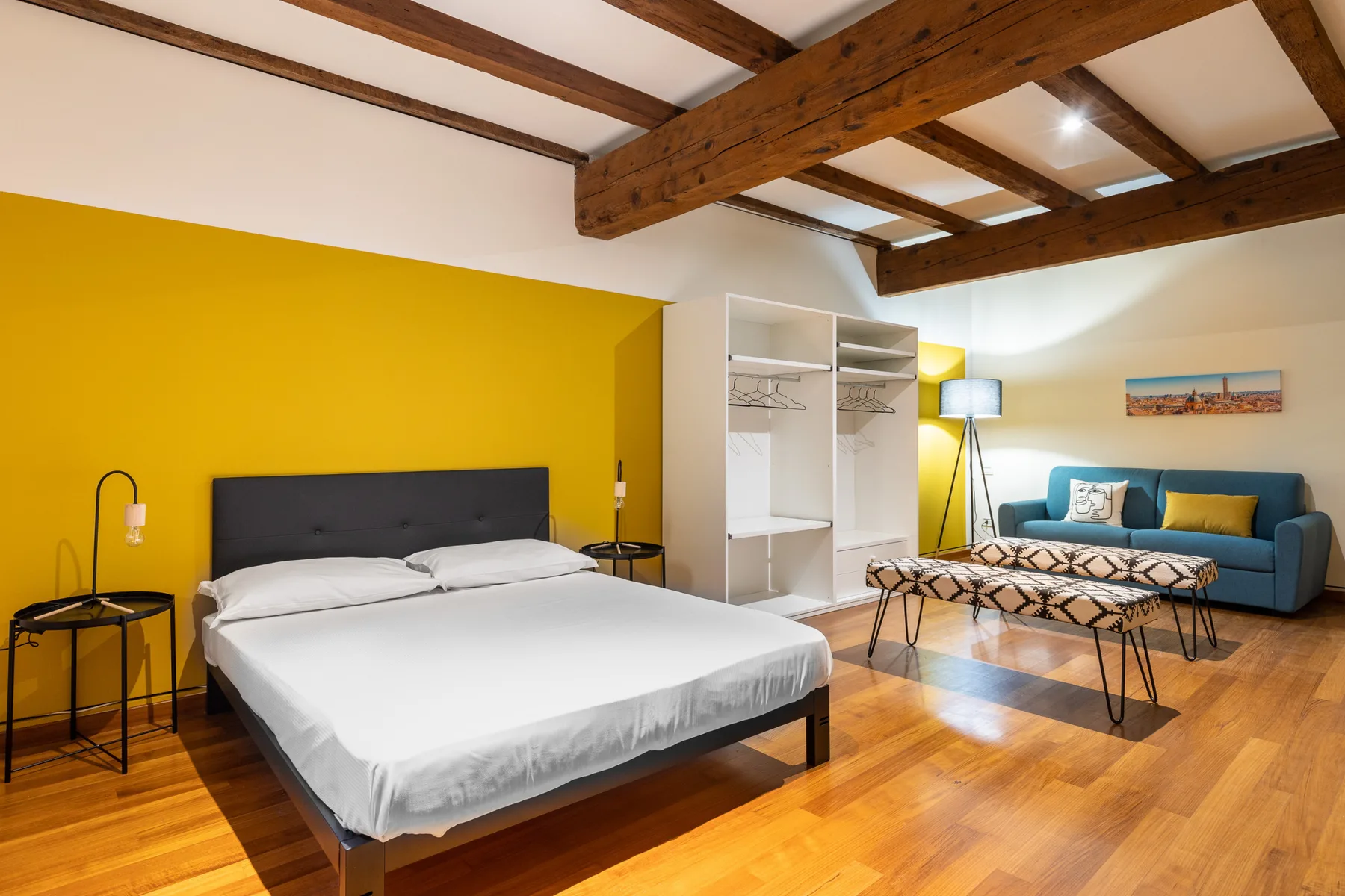 Un dormitorio con una cama grande, un armario abierto y una zona de estar bajo vigas vistas.
