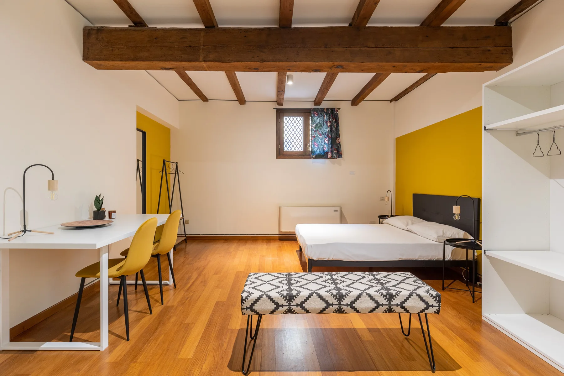 Un dormitorio con cama, escritorio y banco bajo vigas de madera expuestas en el techo.
