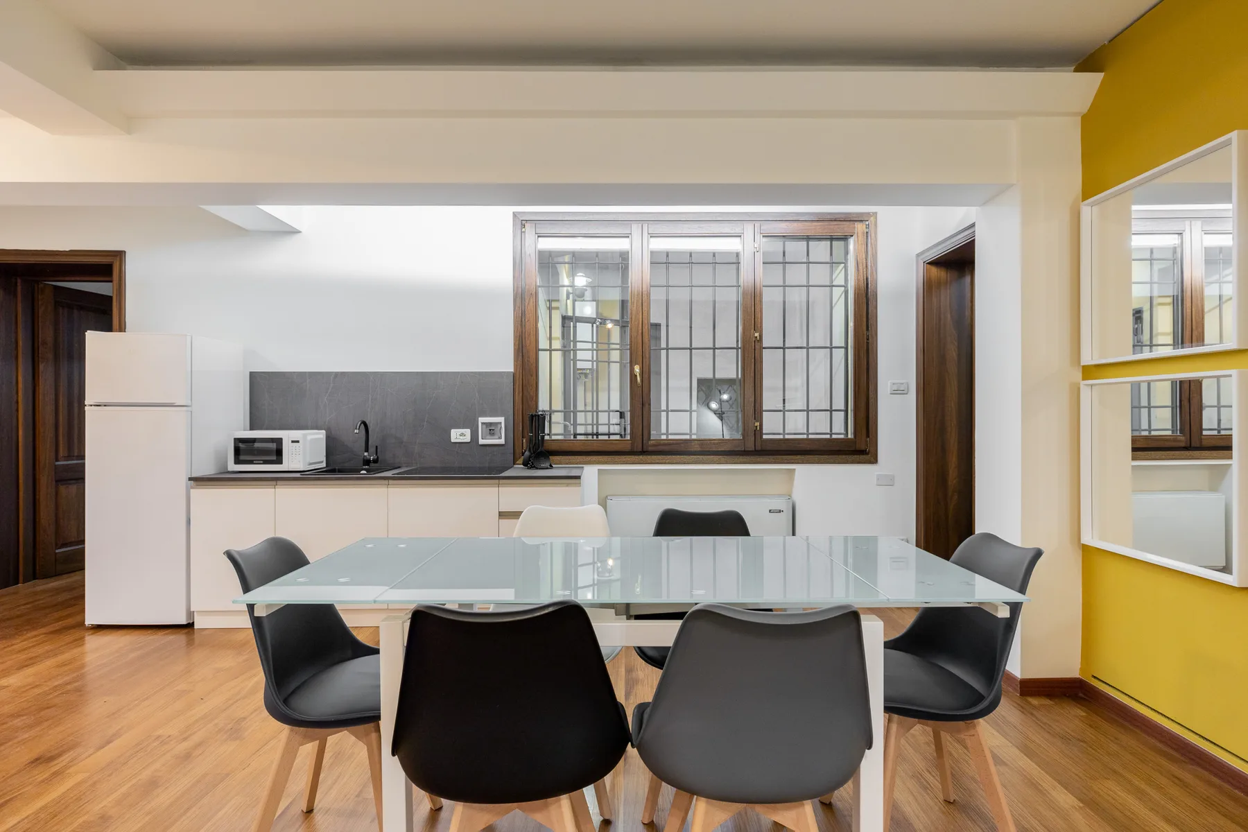 Un comedor con mesa de vidrio y asientos junto a una cocina.