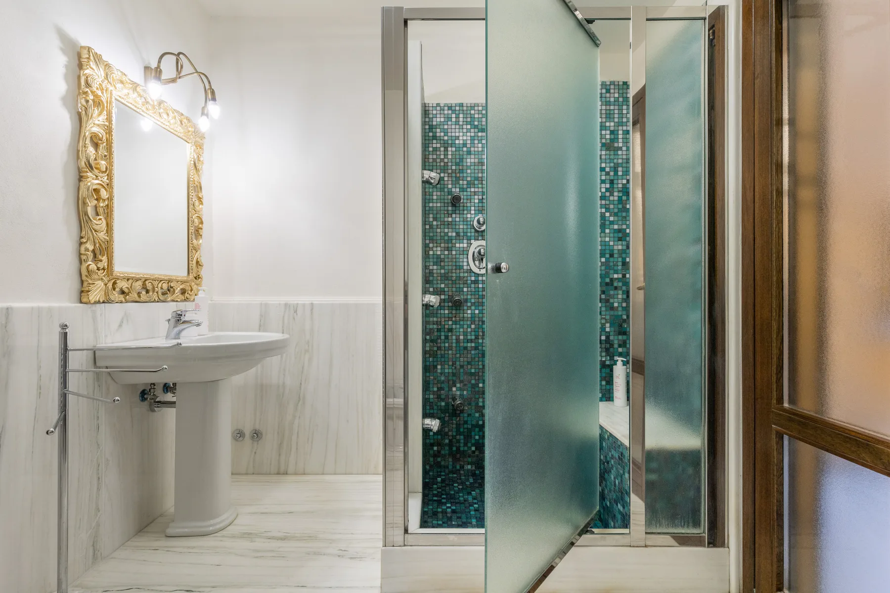 Un baño con lavabo de pedestal, espejo ornamentado y ducha de vidrio.