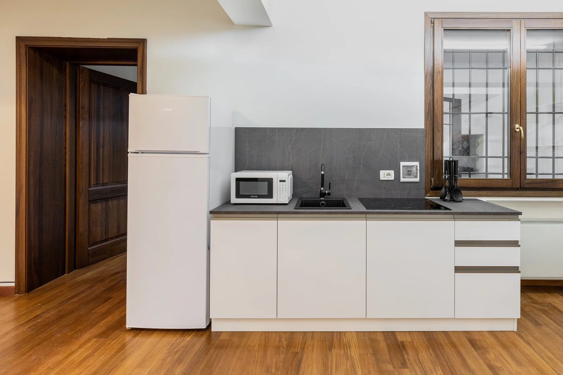 Una cocina compacta con gabinetes blancos, un refrigerador y una encimera.