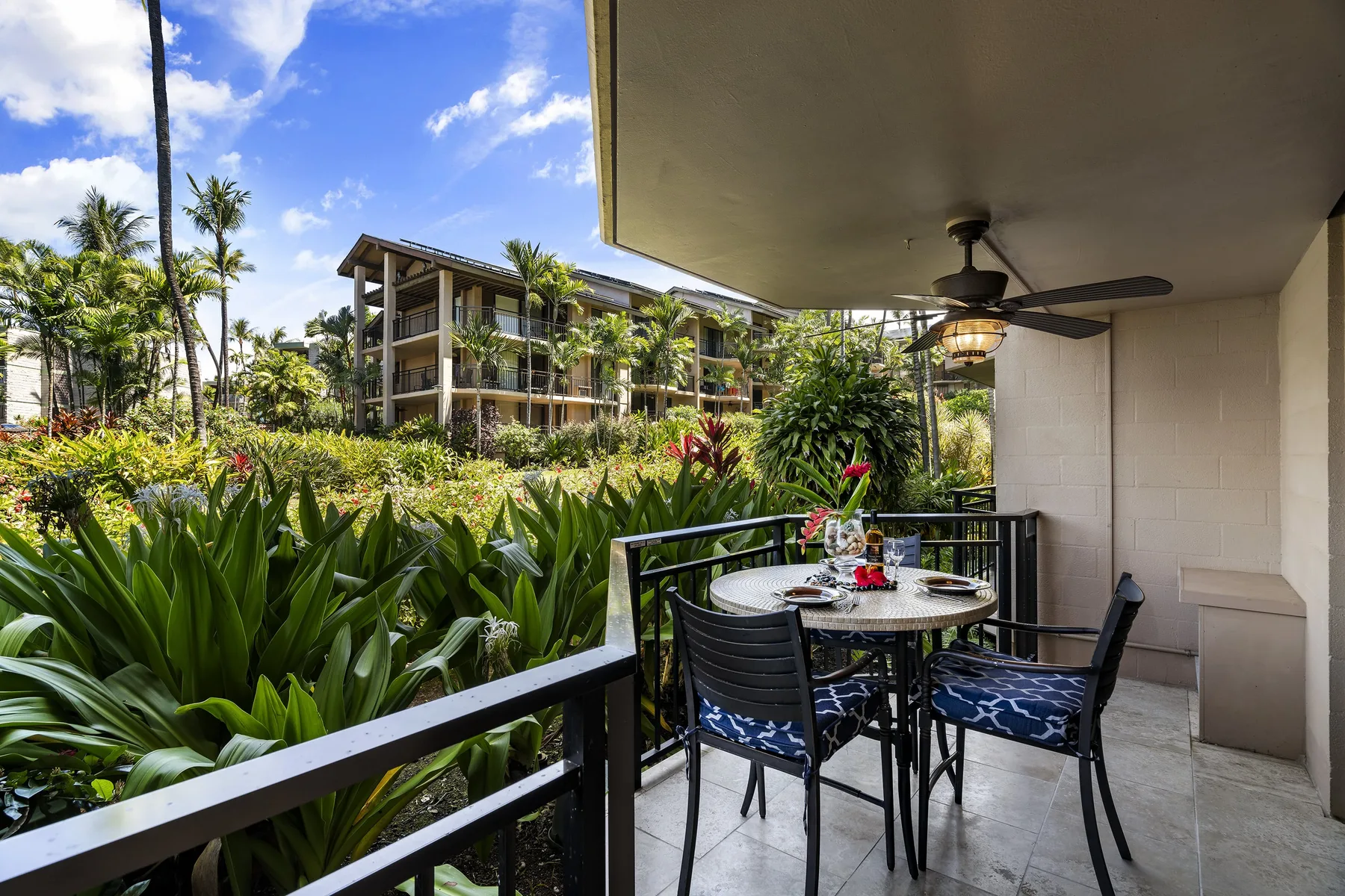 Un patio cubierto tiene una mesa y sillas con vistas a exuberantes jardines tropicales.