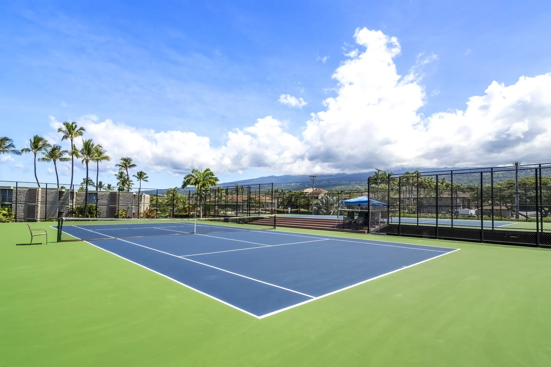 Una cancha de tenis al aire libre con superficie azul y zonas verdes bajo un cielo nublado.