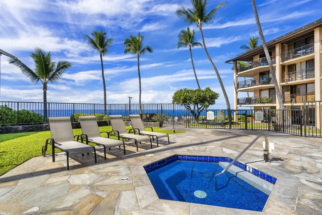 Una zona de piscina al aire libre con asientos, palmeras y vista al mar.