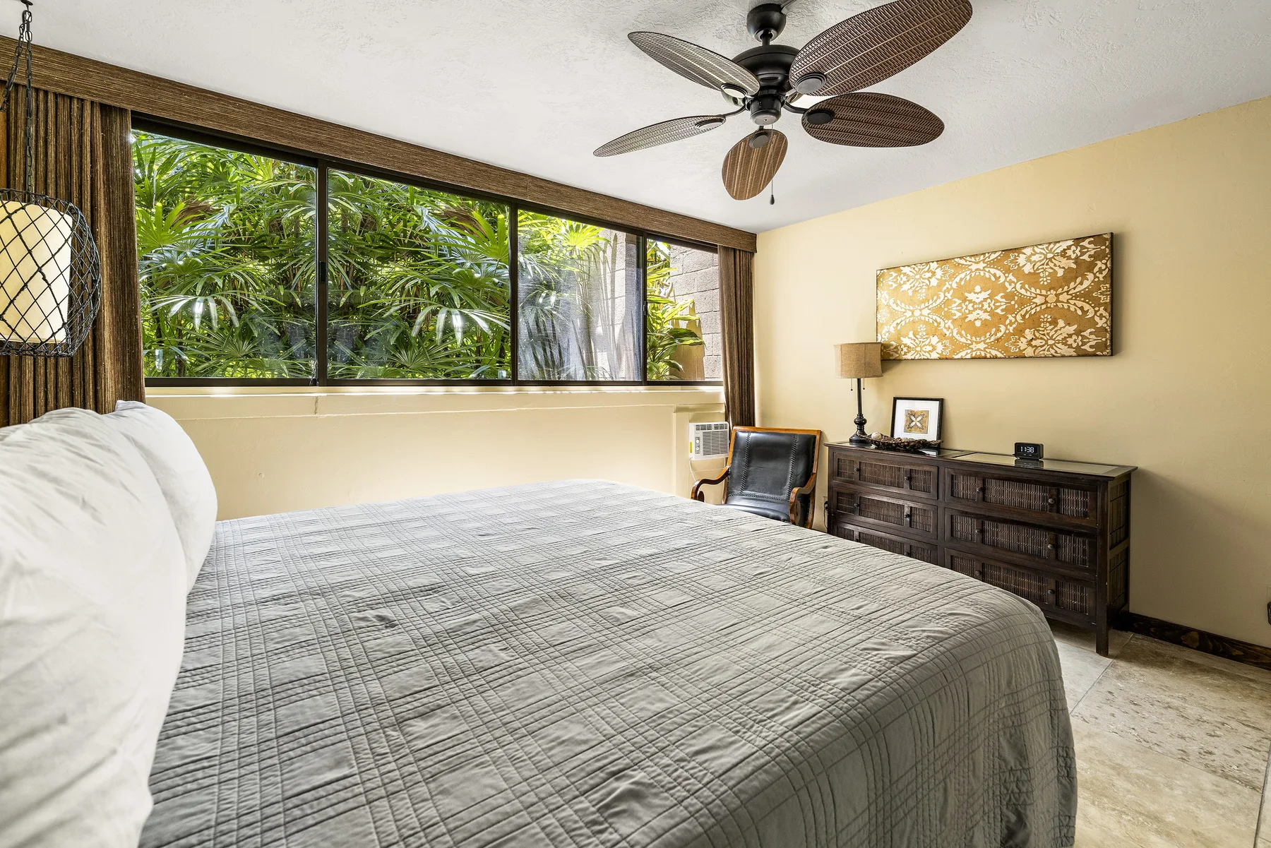 Un dormitorio con una cama bajo amplias ventanas que dan a vegetación frondosa.