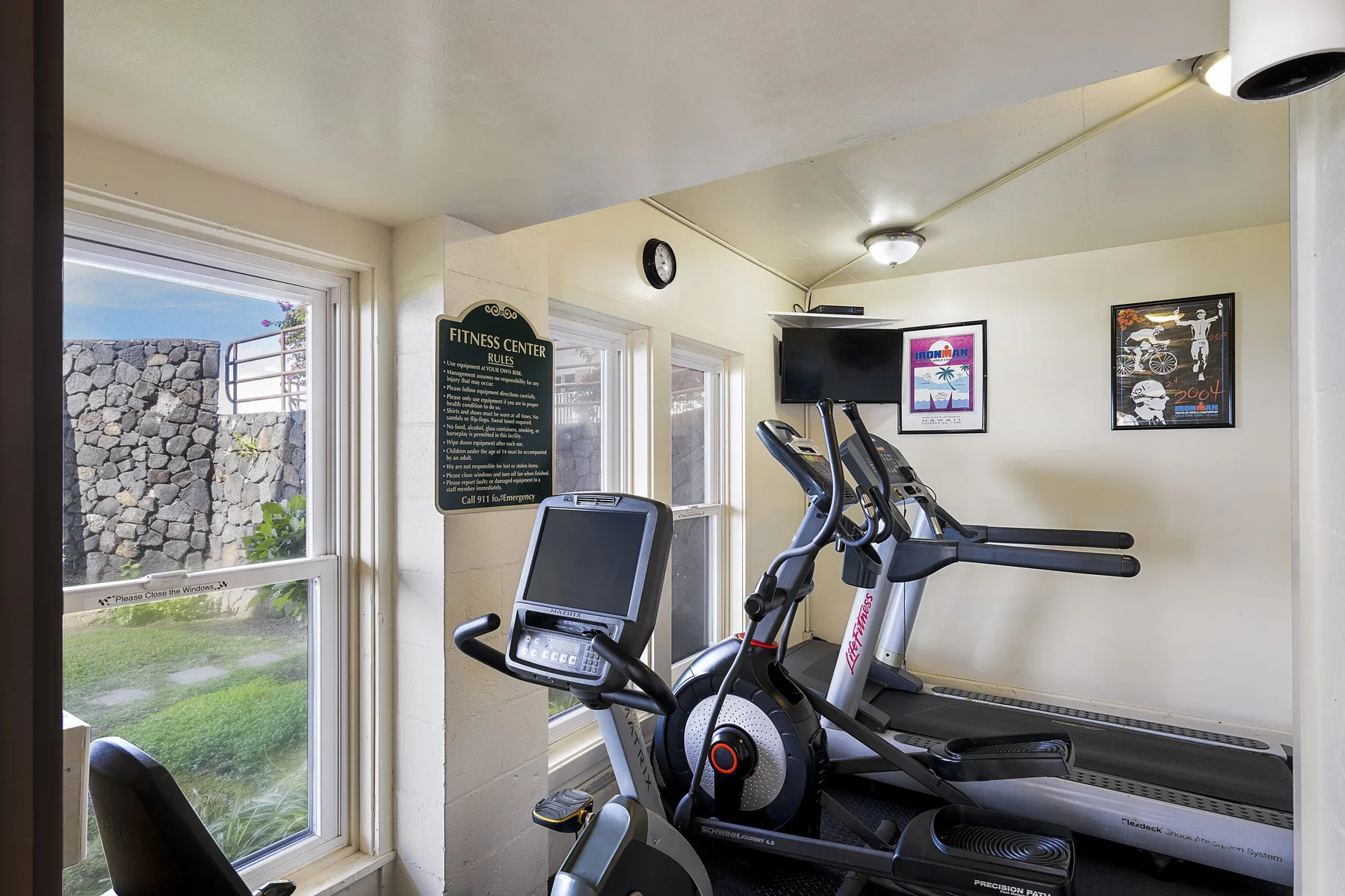 Un pequeño gimnasio con máquinas de ejercicio junto a grandes ventanas.
