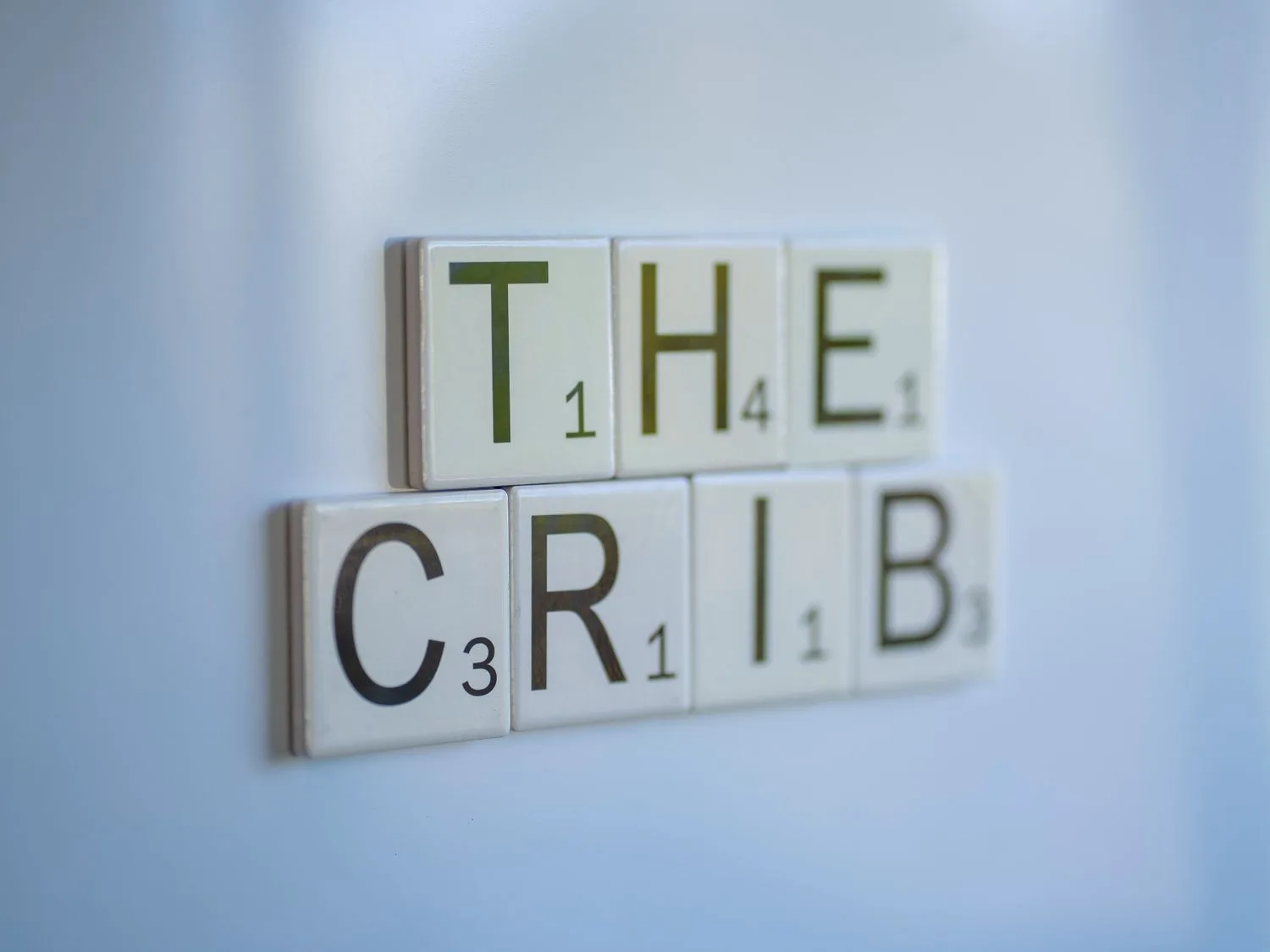 Fichas de Scrabble forman “THE CRIB” sobre un fondo liso de color claro.