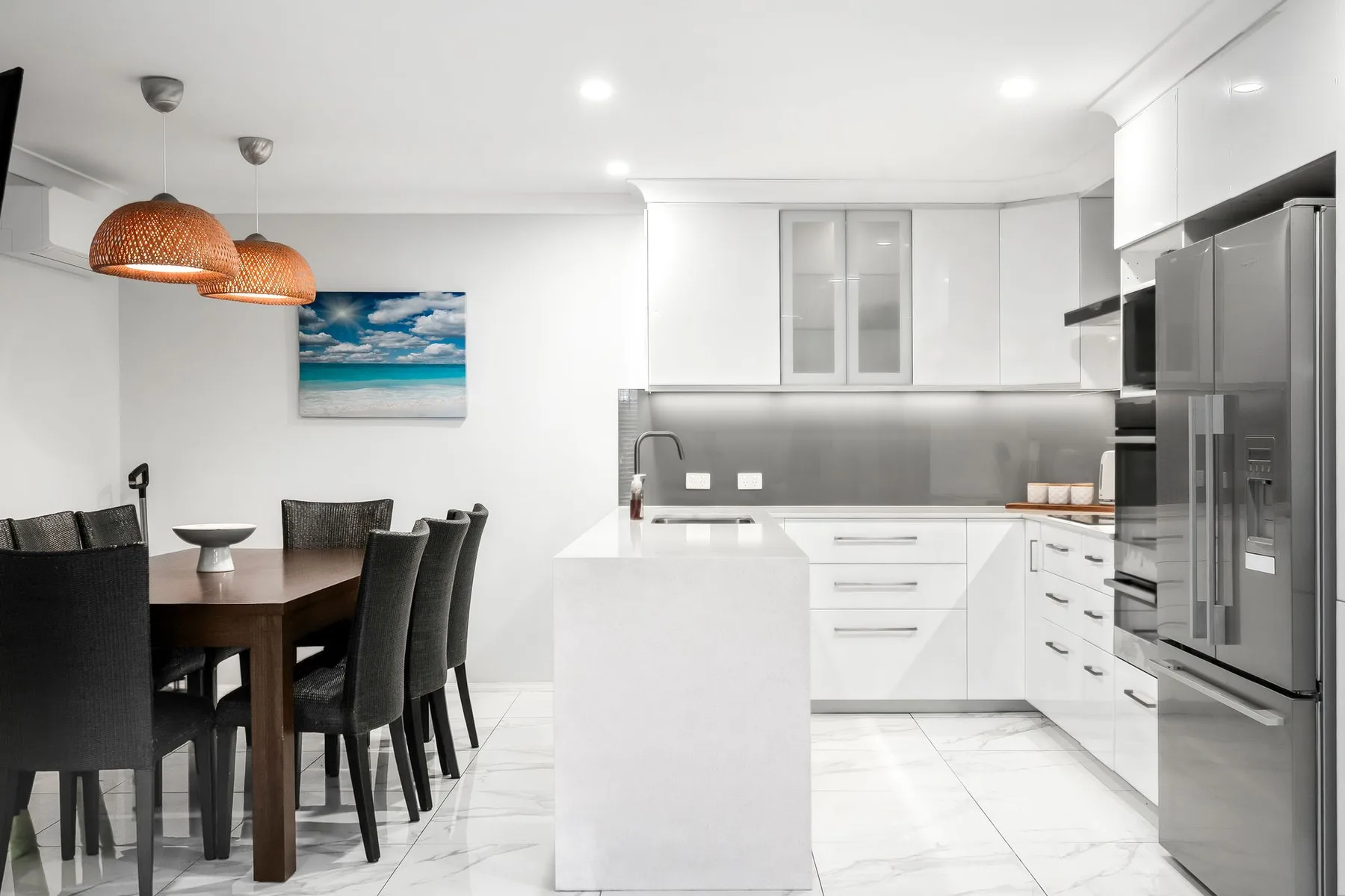 Una cocina y comedor luminosos con gabinetes blancos y una mesa oscura.