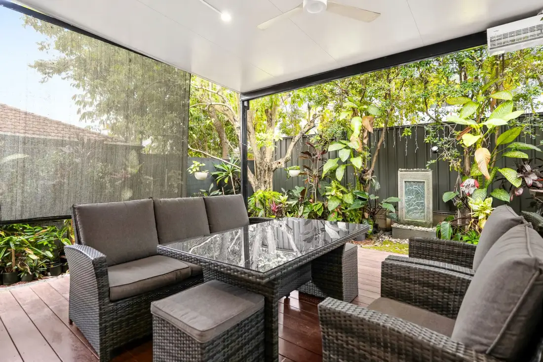 Una zona de estar exterior cubierta con una mesa de vidrio y vegetación alrededor.
