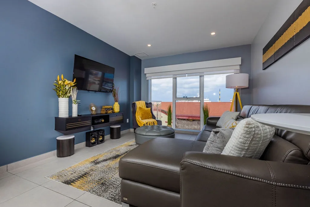 Your stylish living space blends calming blue walls, plush gray seating, and pops of cheerful yellow. Sink into the sofa, stream your favorite shows, and gaze out at neighborhood views framed by bright windows.