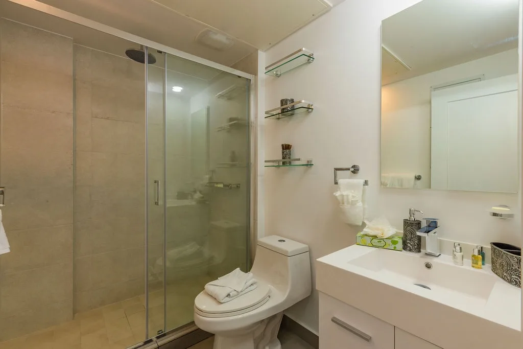 Step into your modern, spotless bathroom with a walk-in glass shower, crisp white vanity, and thoughtful touches like fresh towels and premium toiletries ready for you.