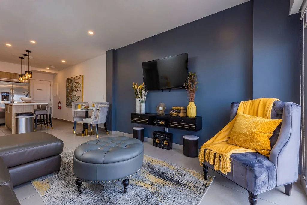 Unwind in this stylish open-concept living space, featuring elegant furnishings in rich greys and golden accents, perfect for your evening relaxation with smart TV entertainment.