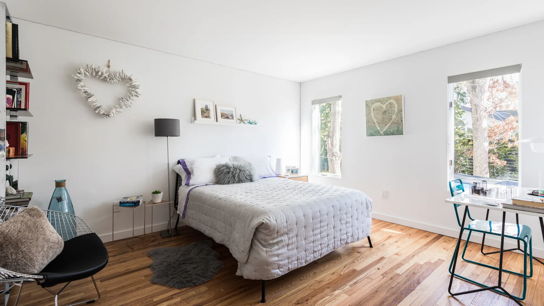 Un dormitorio luminoso con una cama, suelo de madera y ventanas grandes.